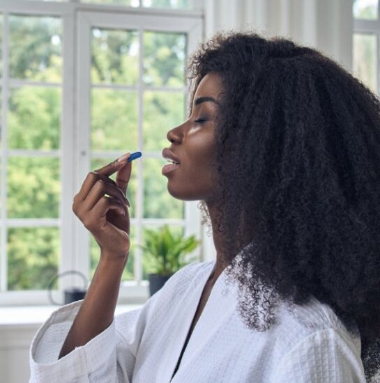 A woman holding a blue pill to her mouth about to take it.