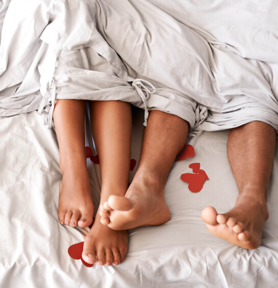 couple laying in bed, showing feet only, with red hearts