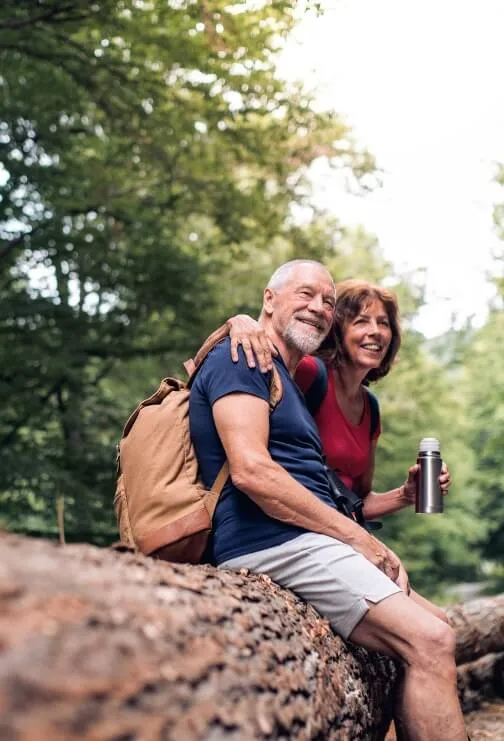 A older couple sitting on a log relaxing from a hike.