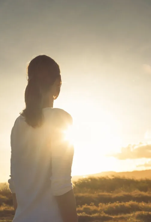 Woman looking off at the sunset in the distance.