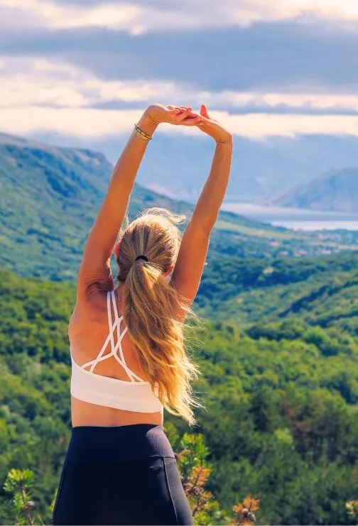 Woman stretching at the top of a mountain looking into the valley